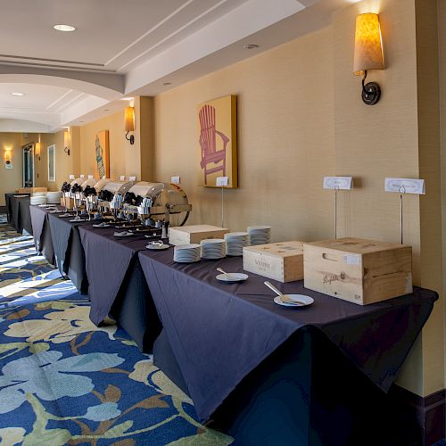 A hallway with catering setup: tables covered in black tablecloths, plates, cups, dispensers, wooden boxes, and wall paintings.