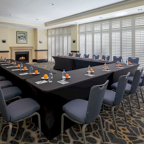 The image shows a conference room setup with tables arranged in a U-shape, chairs, notepads, bottles of water, and oranges on each setting.