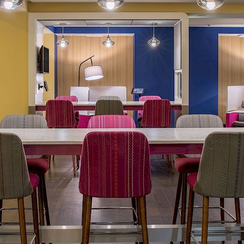 A modern, brightly colored workspace with tables, chairs, mounted screens, and hanging lamps in a stylishly designed interior.