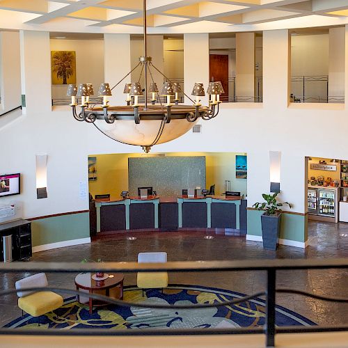A hotel lobby with a circular design, reception desk, seating area, chandelier, and decorative carpet, all under soft, warm lighting.