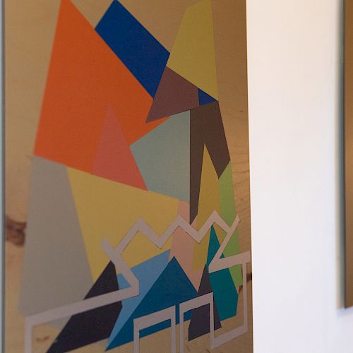 Two abstract paintings with geometric shapes and various colors are displayed on a white wall.