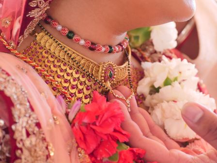 A close-up of a person wearing ornate jewelry, including a gold necklace and a beaded necklace, adorned with flowers.