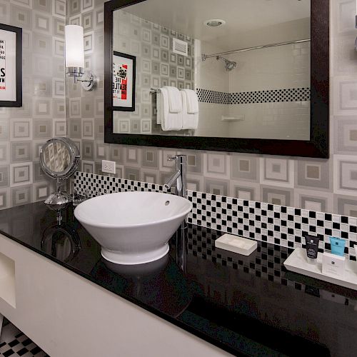 A modern bathroom with a round sink, large mirror, and Beatles-themed decor. The black and white checkered pattern accents the sleek design.