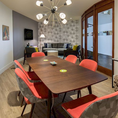 A modern conference room with a wooden table, red cushioned chairs, abstract art on the walls, and a contemporary chandelier ends the sentence.