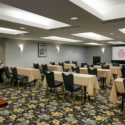 The image shows a conference room with tables and chairs arranged for a seminar or meeting. A projector screen displays the Crowne Plaza logo.