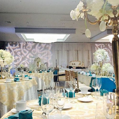 This image shows an elegant banquet hall setup with decorated tables, floral arrangements, glassware, and napkins, suggesting a formal event or celebration.